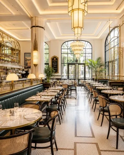 La salle d'une brasserie, banquettes vertes et tables dressées sous les lustres.